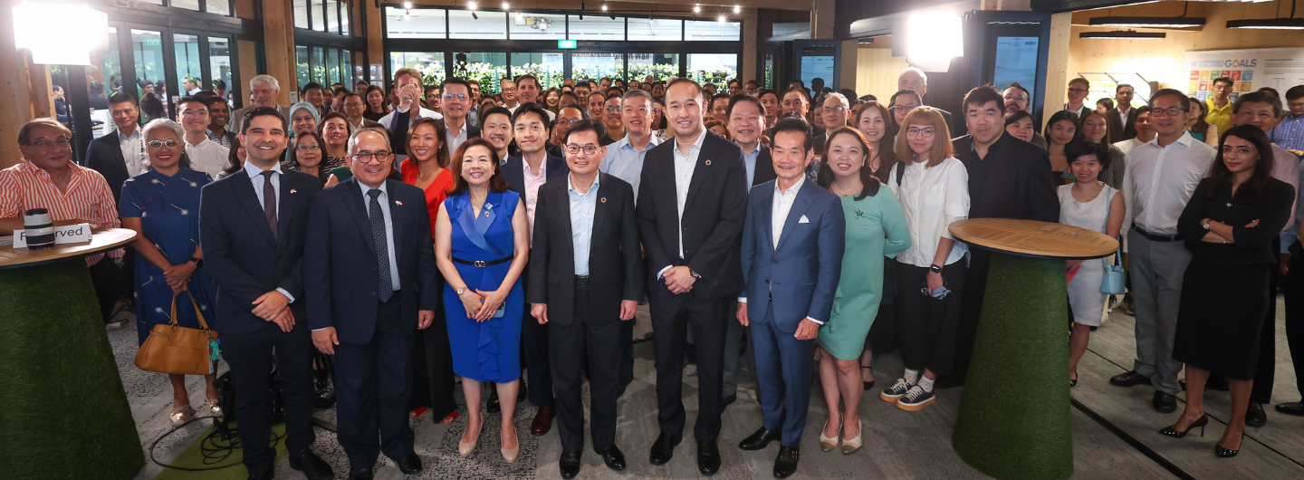 Large group of people posing indoors, some in suits and dresses. SDG poster visible.